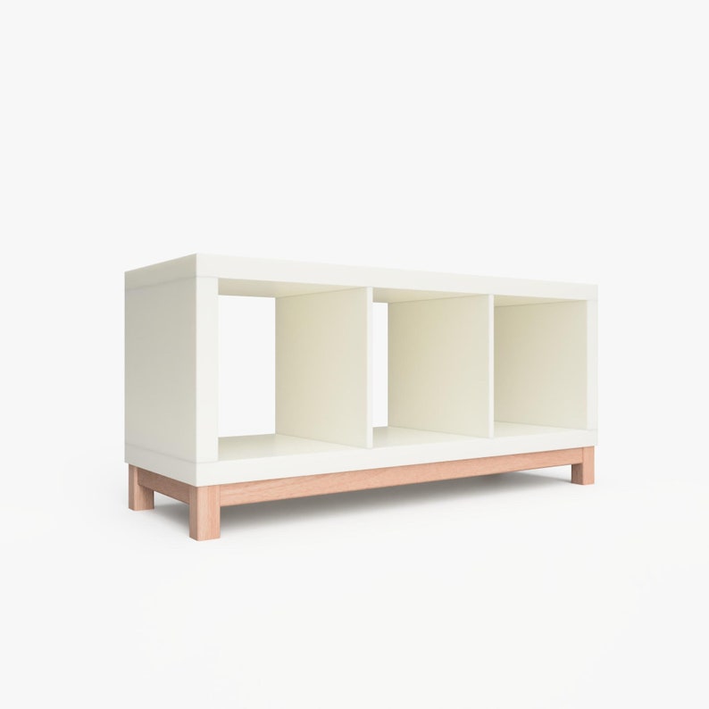 May include: White bookshelf with three open cubbies and a natural wood base. The bookshelf is made of wood and has a modern design.