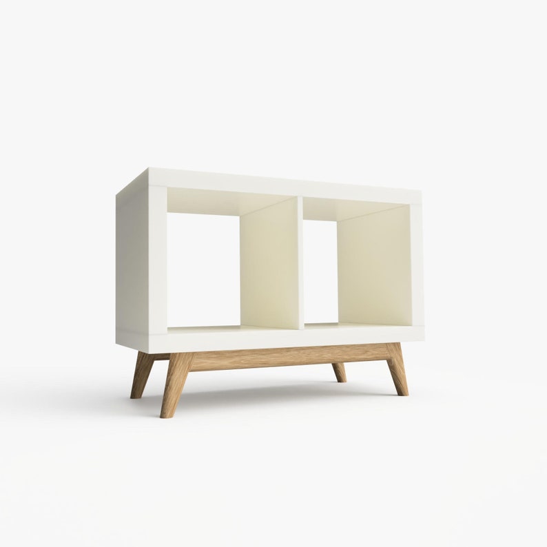 May include: White bookshelf with two open shelves and a wooden base. The bookshelf has a modern design with angled legs.