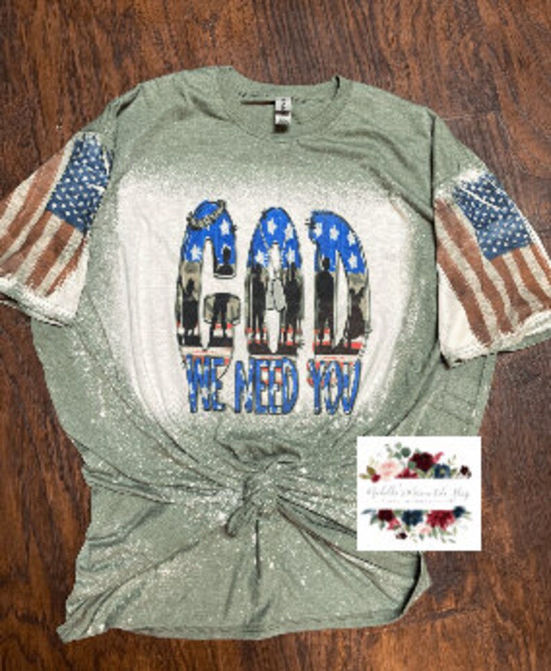 May include: Green t-shirt with a bleached design featuring the words "God We Need You" and an American flag on each sleeve.