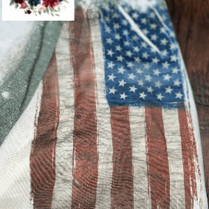 May include: A distressed American flag design printed on a light green t-shirt. The flag is faded and has a worn look, with red and white stripes and blue stars.