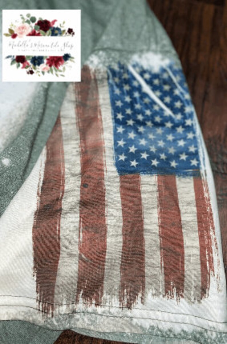 May include: A distressed American flag design printed on a light green t-shirt. The flag is faded and has a worn look, with red and white stripes and blue stars.