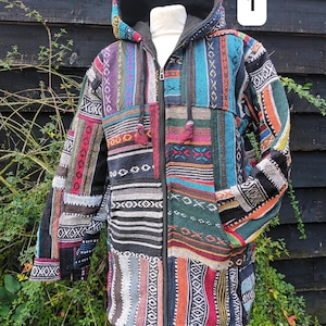 May include: A hooded patchwork jacket with a variety of colourful fabric patterns. The jacket has a full-length zip, two pockets, and decorative tassels. The background is a dark wooden fence and green foliage.