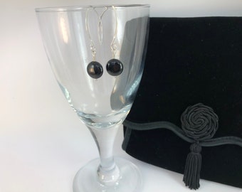 May include: A pair of silver dangle earrings with black round beads. The earrings are hanging from a glass.