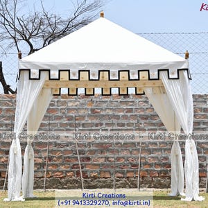 May include: A white square canopy tent featuring a peaked roof and a decorative black and gold scalloped valance. The structure includes four corner posts topped with gold finials and white fabric curtains tied back at each corner.