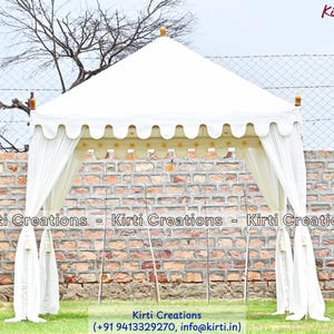 May include: A white square canopy tent featuring a scalloped valance with gold star accents along the edges. The structure has four corner posts topped with small wooden finials and white fabric curtains tied back at each corner of the frame.