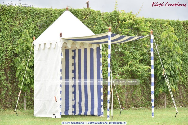 May include: A white and blue striped canopy tent with a white canvas roof. The tent is set up outdoors with a green lawn and a hedge in the background. The tent has a white fabric awning and is supported by wooden poles.