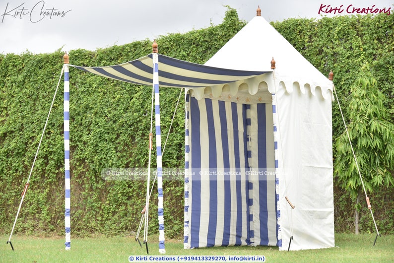 May include: A white and blue striped canopy tent with a white canvas roof. The tent is set up in a grassy area with a green hedge in the background. The tent has a white fabric awning with blue stripes.
