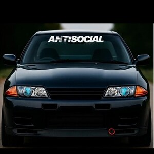 May include: A black sports car with the word "ANTISOCIAL" in white across the windscreen. The car has blue headlights and a red tow hook. The image is a front view of the vehicle.