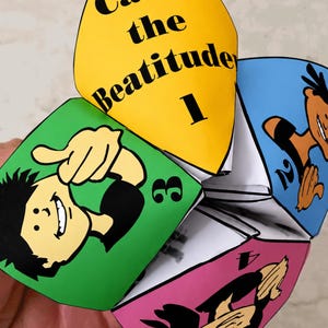 May include: A colorful paper fortune teller with the text "Call the Beatitude 1" on a yellow panel. Other panels are green, blue, and pink, each with a cartoon illustration and a number. The fortune teller is held in a person's hand.