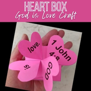 Puede incluir: Caja artesanal en forma de corazón rosa con las palabras "Dios es amor" y "1 Juan 4:8" en ella.