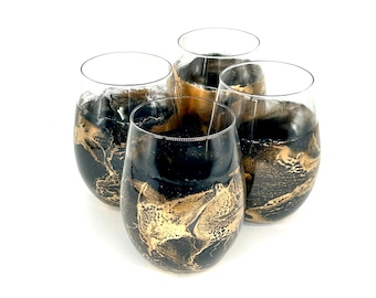 May include: Four clear glass wine glasses with black and gold marbled designs. The glasses are arranged in a circle on a white background.