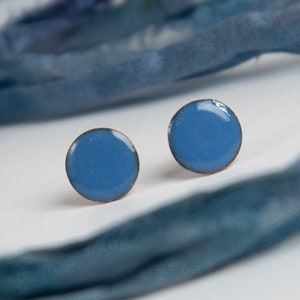 Op de afbeelding: Een paar kleine, ronde, blauwe oorbelletjes. De oorbelletjes zijn gemaakt van metaal en hebben een gladde, glanzende afwerking.