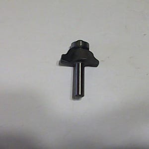 May include: A dark metal router bit with a cylindrical shaft and a multi-faceted cutting head. The bit is designed for woodworking and shaping edges. The tool is shown against a white background.