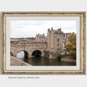 May include: A photograph of a stone bridge over a river in Bath, England. The bridge is lined with buildings and trees. The sky is overcast.