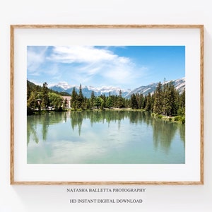 May include: A scenic photograph of a lake with snow-capped mountains in the background. The lake is surrounded by trees and reflects the blue sky and clouds.