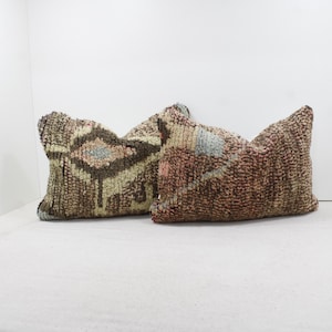 Puede incluir: Dos almohadas decorativas con un patrón geométrico marrón, beige y azul. Las almohadas están hechas de una tela suave y tejida.