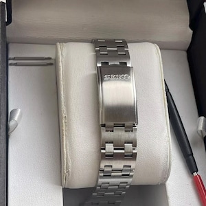 May include: A silver watch band with the word "SEIKO" printed on the clasp.