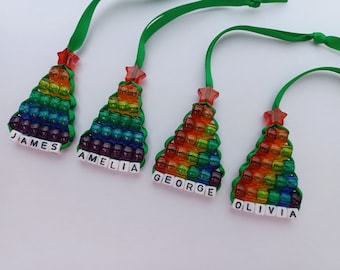 May include: Four rainbow beaded Christmas tree ornaments with green ribbon and personalized names: James, Amelia, George, and Olivia.