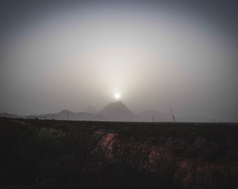 Puede incluir: Una vista brumosa y distante de una cordillera con el sol brillando a través de las nubes. Las montañas se recortan contra el cielo brillante.