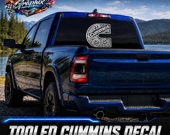 Puede incluir: Una calcomanía de vinilo blanca que presenta una letra C estilizada con un intrincado patrón floral y el texto cummins en su interior, aplicada en la ventana trasera de una camioneta azul oscuro cerca de un lago y un bosque.