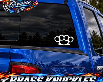 Puede incluir: Un adhesivo de vinilo blanco con forma de puño americano aplicado en la ventana trasera de una camioneta azul. El diseño muestra la forma clásica de cuatro orificios con un área de agarre redondeada sobre el cristal tintado del vehículo.