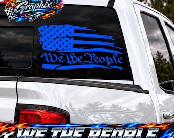 Puede incluir: Un adhesivo de vinilo azul para ventana que presenta un diseño de bandera estadounidense desgastada con el texto We the People en una fuente cursiva estilizada. El adhesivo está aplicado en la ventana trasera de una camioneta blanca.