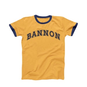 May include: A yellow t-shirt with a navy blue ringer and the word "BANNON" printed in navy blue across the front.