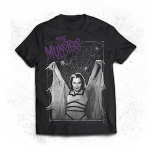 May include: Black t-shirt with a graphic of a woman with long, flowing hair and a spiderweb behind her. The text "THE MUNSTERS" is printed in purple above the graphic.