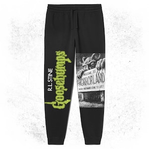 May include: Black sweatpants featuring a green Goosebumps logo and a graphic print of a monster holding a sign that reads "Welcome to Horrorland, Where Nightmares Come to Life!"