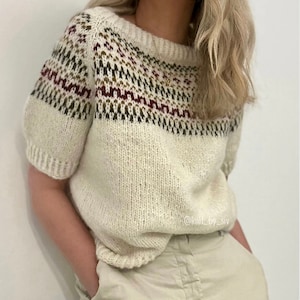 Può includere: Un maglione di lana bianco con un motivo geometrico colorato intorno al collo. Il maglione ha maniche corte e una vestibilità comoda.