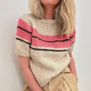 May include: A beige short-sleeved sweater with pink and brown stripes. The sweater is knitted and has a relaxed fit.