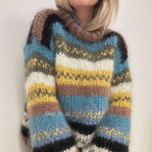 May include: A cozy, oversized sweater with a high neck, featuring horizontal stripes in various colors. The color palette includes shades of blue, yellow, brown, white, and black. The sweater has a textured, fluffy appearance, suggesting a warm, knitted design.
