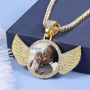 Op de afbeelding: Gouden ketting met een hanger met een foto van een vrouw en een kind. De hanger is omringd door heldere strass steentjes en heeft aan beide kanten twee vleugels.
