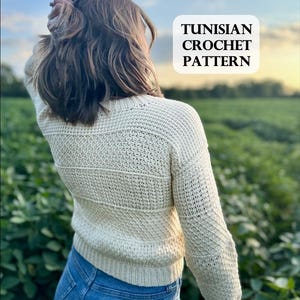 以下が含まれることがあります： 長袖のクリーム色のチュニジア式かぎ針編みのセーターを着た女性。セーターは質感のあるステッチパターンになっています。画像に「TUNISIAN CROCHET PATTERN」というテキストが重ねられています。