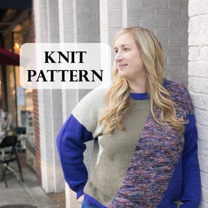 May include: A knit pattern is displayed on a sign in front of a woman wearing a color-blocked sweater. The sweater features blue, white, and olive green panels with a diagonal section of multicolored yarn. The woman is wearing blue jeans.