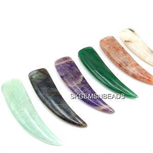 May include: A collection of six polished gemstone pendants in various colors, including green, purple, and orange. Each pendant has a curved, elongated shape, and the gemstones are displayed against a white background.