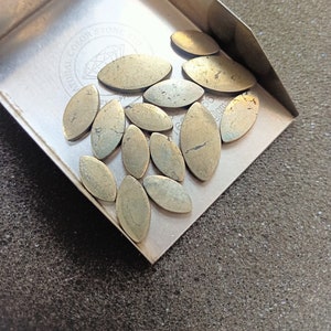 May include: A collection of 14 gold-toned, oval-shaped, pyrite stones in a metal tray. The stones have a rough, textured surface and are arranged in a random pattern.