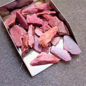 Peut inclure: Un petit plateau en métal rempli d'un tas de pierres précieuses de rubis roses brutes.