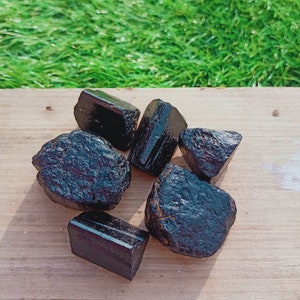 May include: A collection of six black tourmaline crystals on a wooden surface. The crystals are various shapes and sizes, with some having a pointed end.