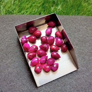 Puede incluir: Una colección de 20 gotas de piedras preciosas rosas en una bandeja de metal. Las piedras preciosas son facetadas y tienen forma de lágrima.