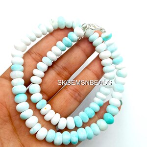 May include: A necklace composed of alternating white and light blue gemstone beads. The beads are oval-shaped and strung together with a silver clasp. The text "SKGEMSNBEADS" is visible in the image.