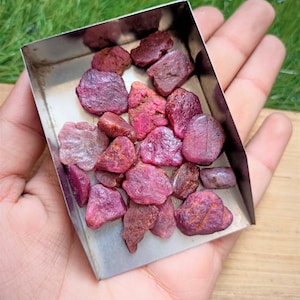 Op de afbeelding: Een klein metalen dienblad gevuld met een verzameling ruwe, roze robijn edelstenen.