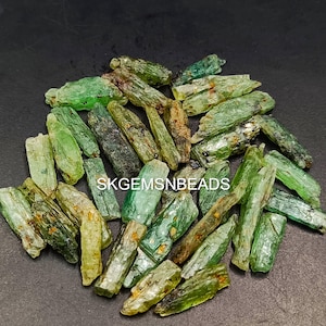 May include: A collection of green and brown rough gemstone points. The points are various sizes and shapes. The points are scattered on a black surface.
