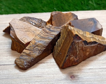 May include: A collection of raw tiger's eye stones, featuring a variety of shapes and sizes. The stones are a mix of brown, gold, and red hues with a shimmering, iridescent effect.