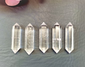 Könnte beinhalten: Fünf klare, doppelt terminierte Quarzkristallspitzen, die in einer horizontalen Reihe angeordnet sind. Jeder Kristall hat eine hexagonale Prismenform mit spitzen Enden auf beiden Seiten und zeigt ein transparentes, glasartiges Aussehen.