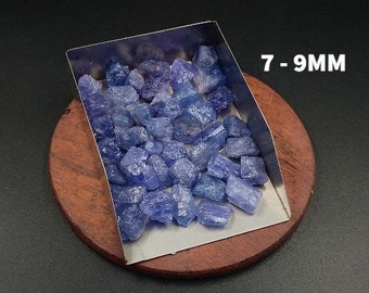 May include: A close-up of a metal scoop filled with blue-purple gemstone chips. The chips are various sizes and shapes, ranging from 7 to 9 millimetres. The scoop is sitting on a wooden surface.