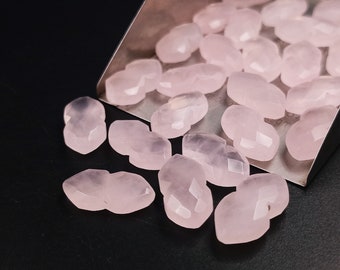 May include: A collection of pink rose quartz beads, each with a faceted, heart-shaped design. The beads are scattered on a silver tray and a black surface.