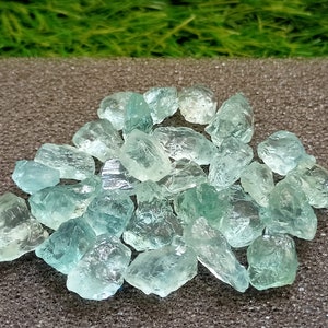 Pode incluir: Um monte de cristais de água-marinha azul claro, alguns com um leve tom verde, sobre um fundo cinza.