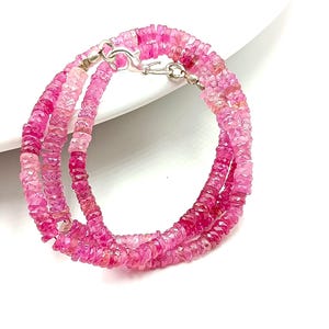 Può includere: Una collana di perle di pietre preziose rosa con una chiusura argentata. Le perle sono sfaccettate e presentano diverse tonalità di rosa.