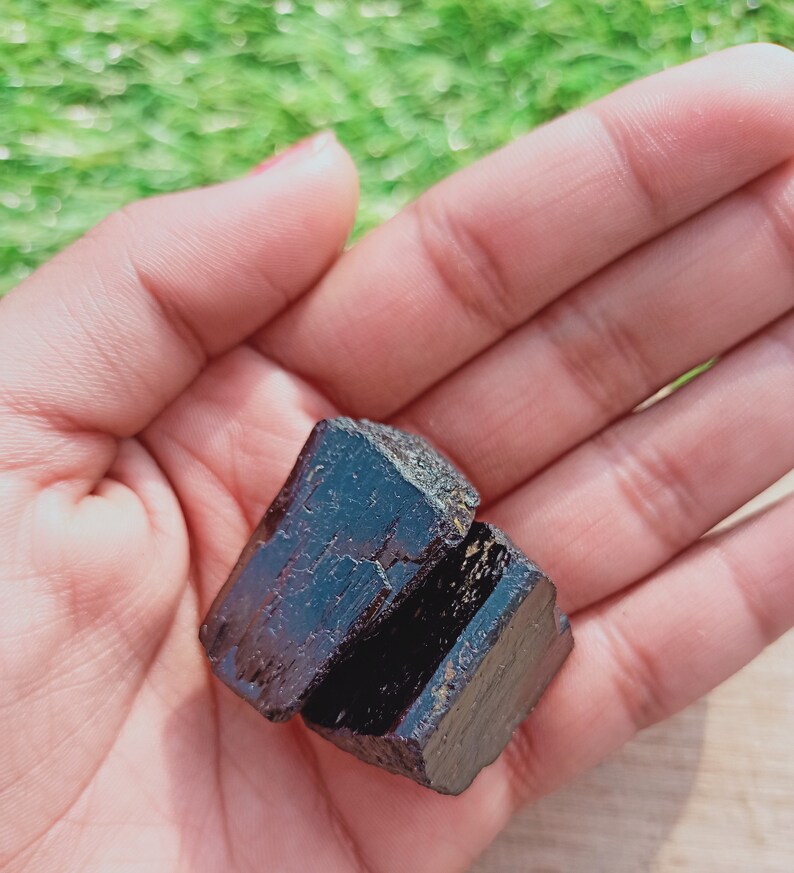 May include: A dark brown, almost black, crystal with a rough, natural texture. The crystal is shaped like a cube and has a slightly iridescent sheen.